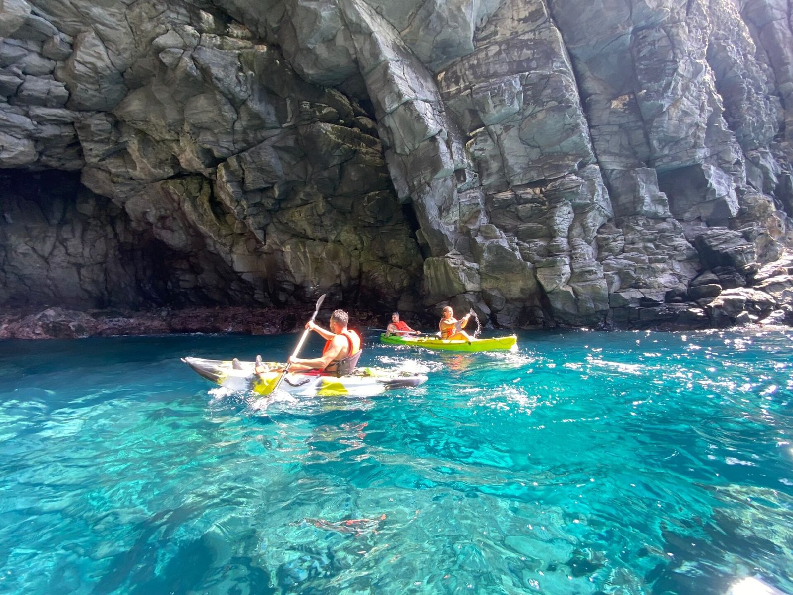 Kayaks sobre agua turquesa a la entrada de una cueva de roca volcánica