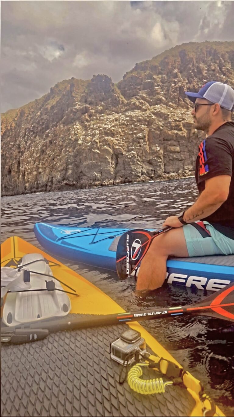 Ezequiel, founder of Adventure Time Tenerife, sitting on a paddle board beside the cliffs