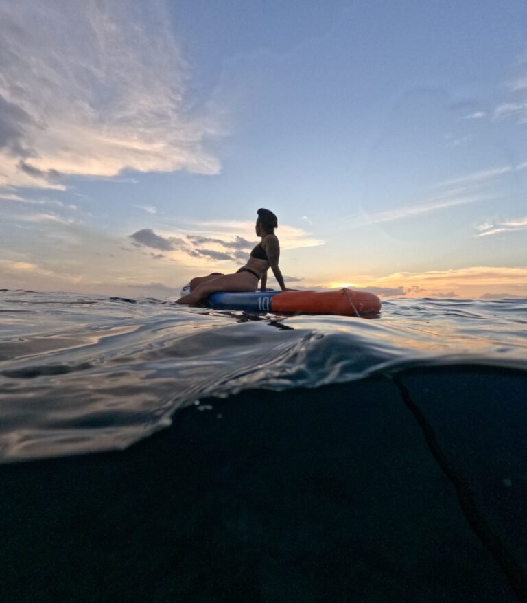 Person sitting on a paddle board with the sun low on the horizon