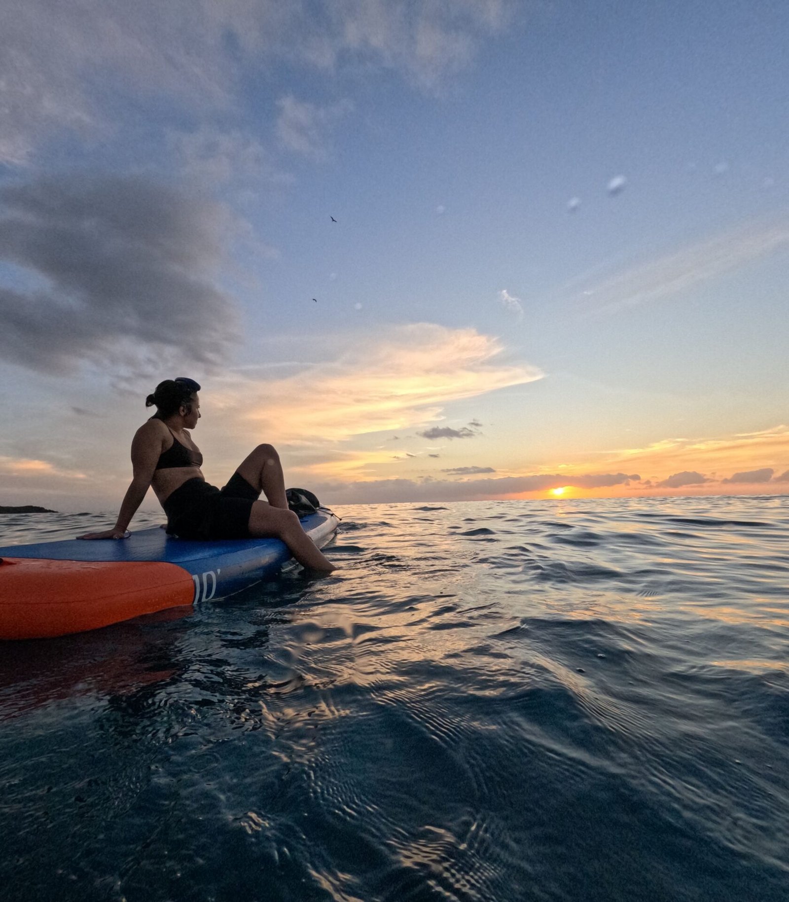 Person sitting on a paddle board at sea at sunset