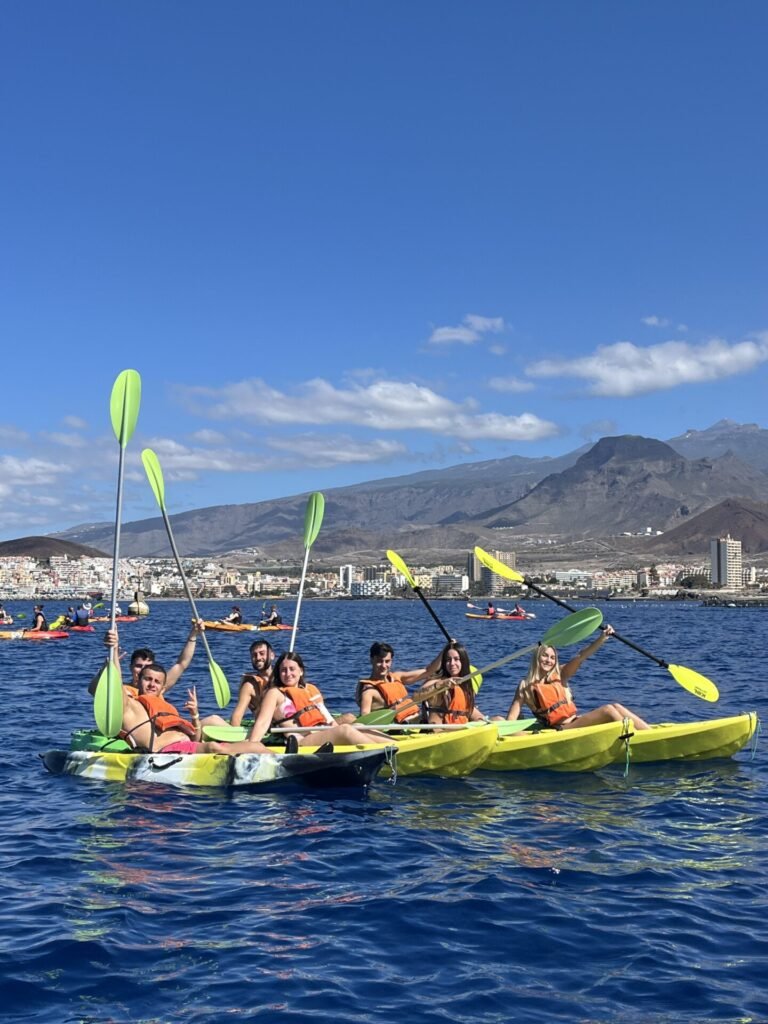 Group raising their paddles in kayaks, with the coast and mountains of Tenerife behind